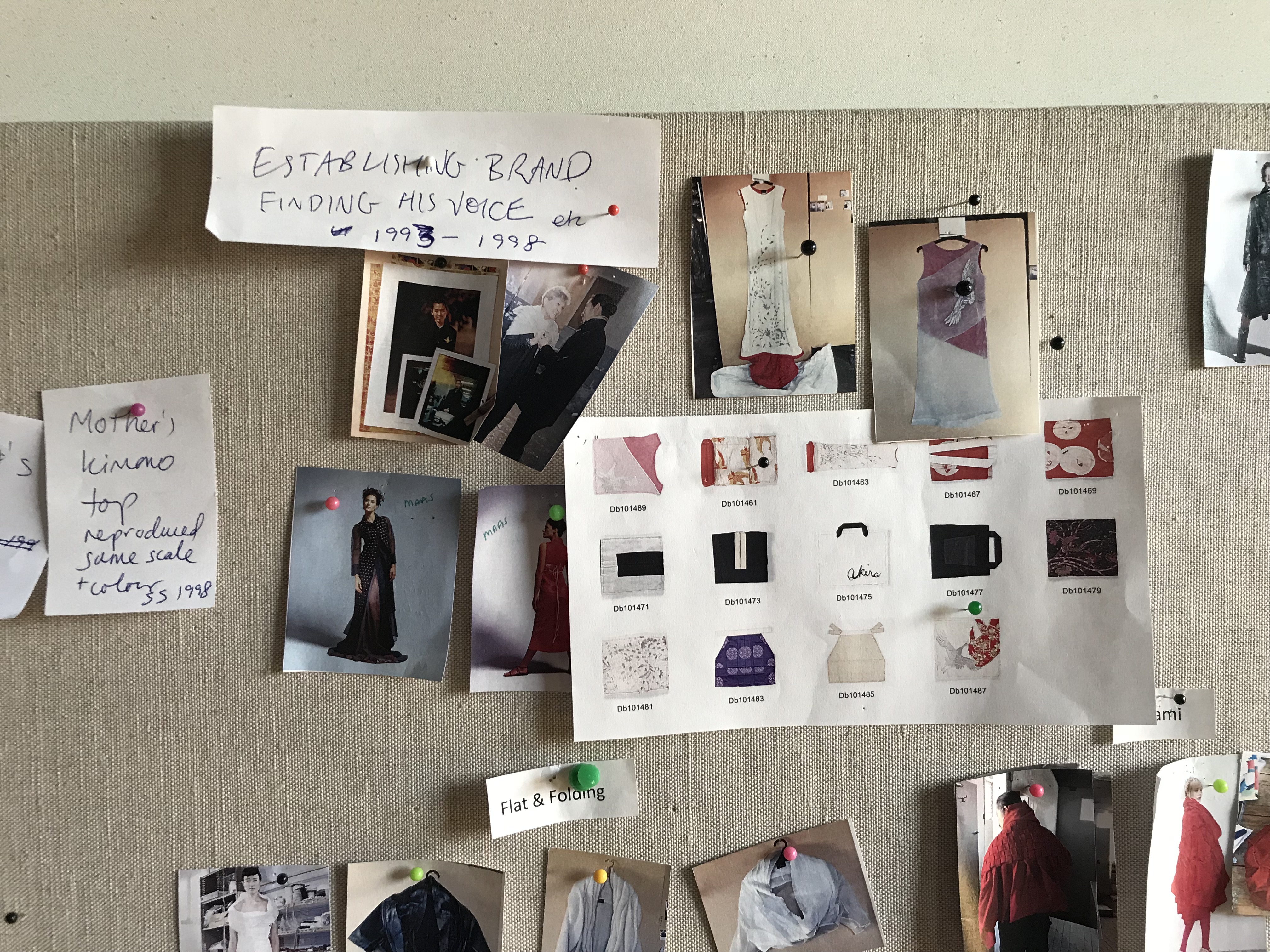 Closeup of a pin-board with handwritten notes and themes, in amongst photographs of garments.